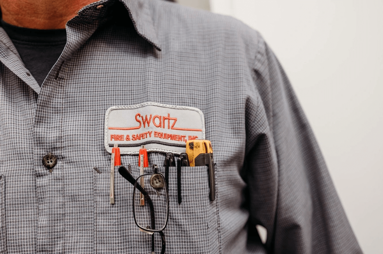Closeup and cropped photo of a fire safety inspector wearing a shirt with the swartz fire safety equipment inc logo above the pocket